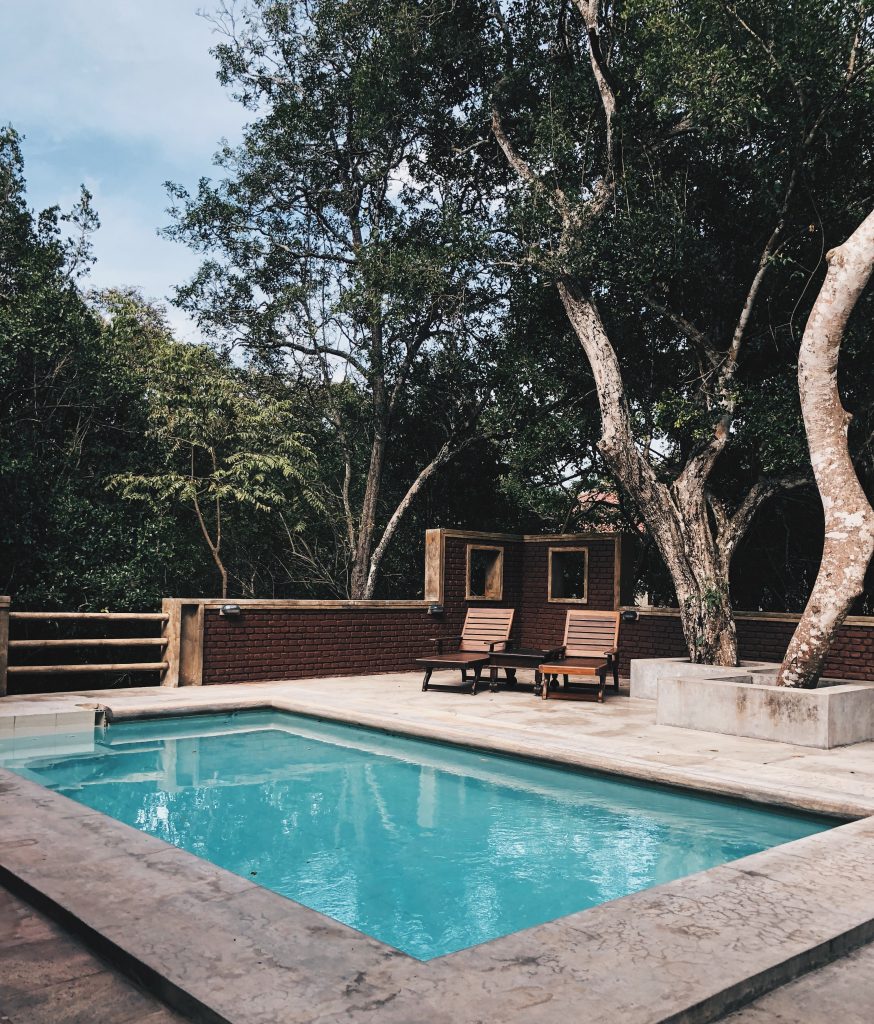 terrasse avec piscine et fauteuils en bois sous les arbres